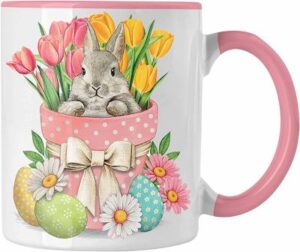 Weiße Tasse mit rosa Henkel und Innenfarbe mit Motiv: Häschen im Blumentopf mit bunten Eiern und Frühlingsblumen