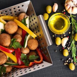 Grillkorb gefüllt mit Gemüse, daneben Ölflasche und Oliven