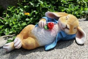 Dekofigur: ein auf dem Rücken schlafender Hase mit Schlappohren, blauer Jacke und einer roten Rose in der Pfote